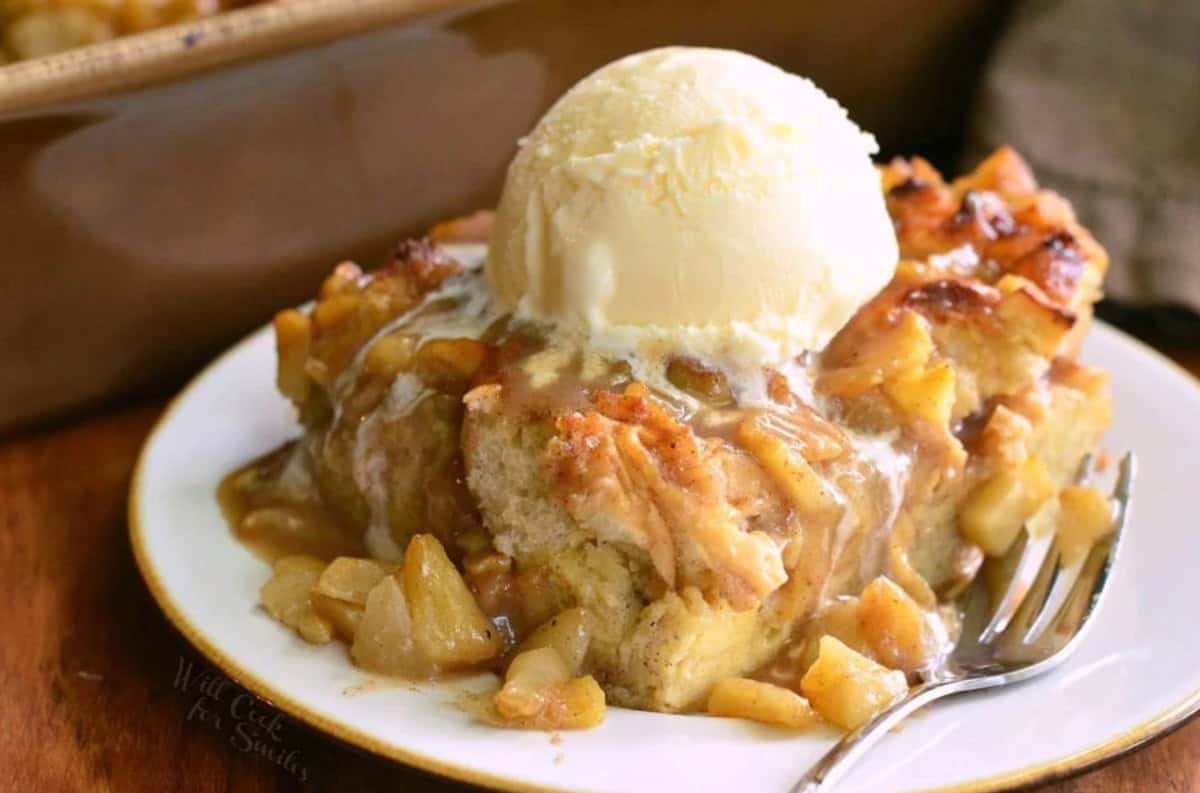 slice of apple pie bread pudding on the plate with ice cream on top and a fork.