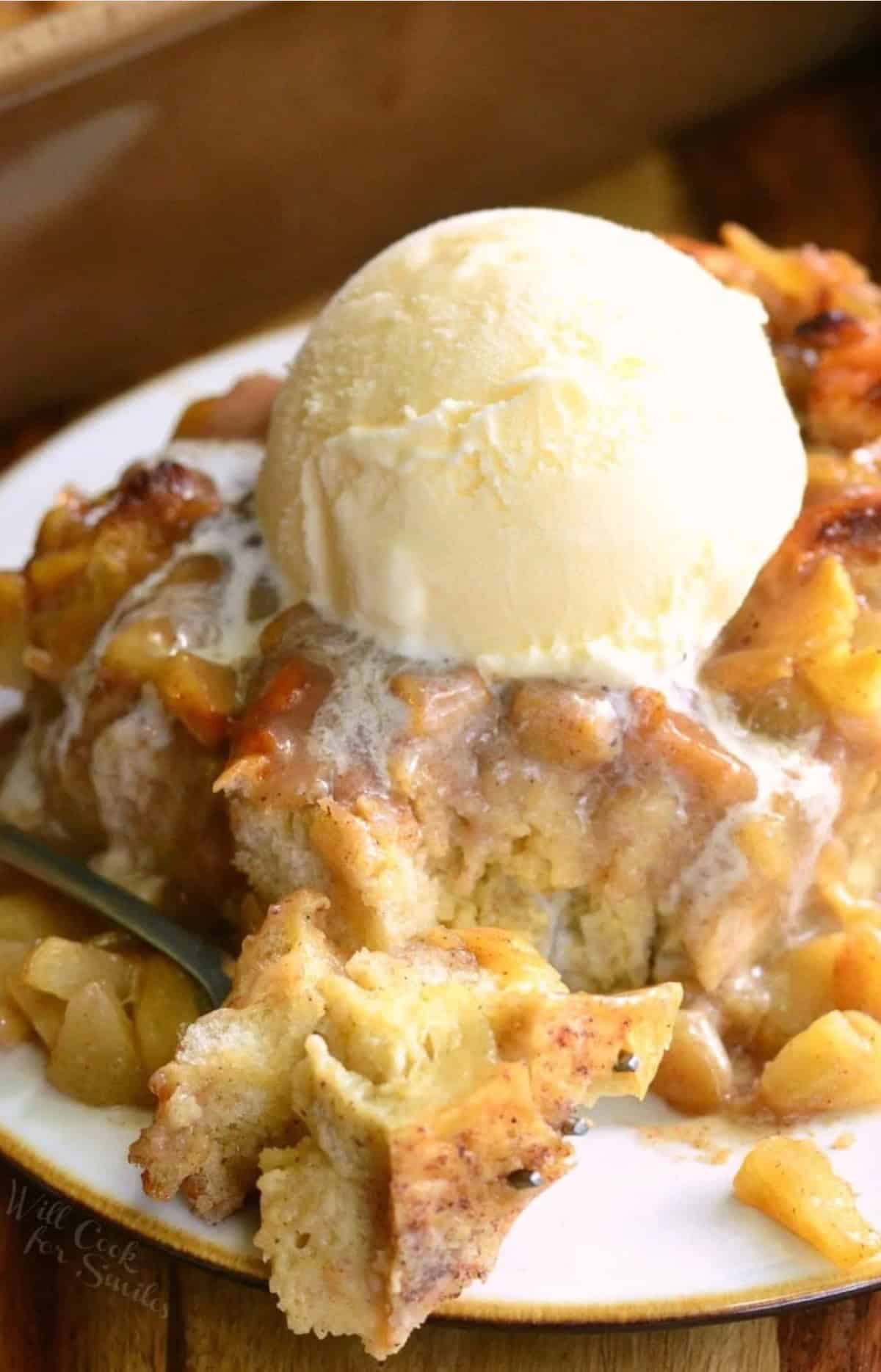 slice of apple pie bread pudding with ice cream on top and a piece taken out with a fork.