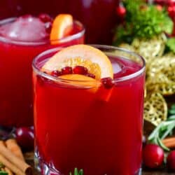 Christmas punch in a glass with another behind with rosemary, cranberries and cinnamon sticks around.