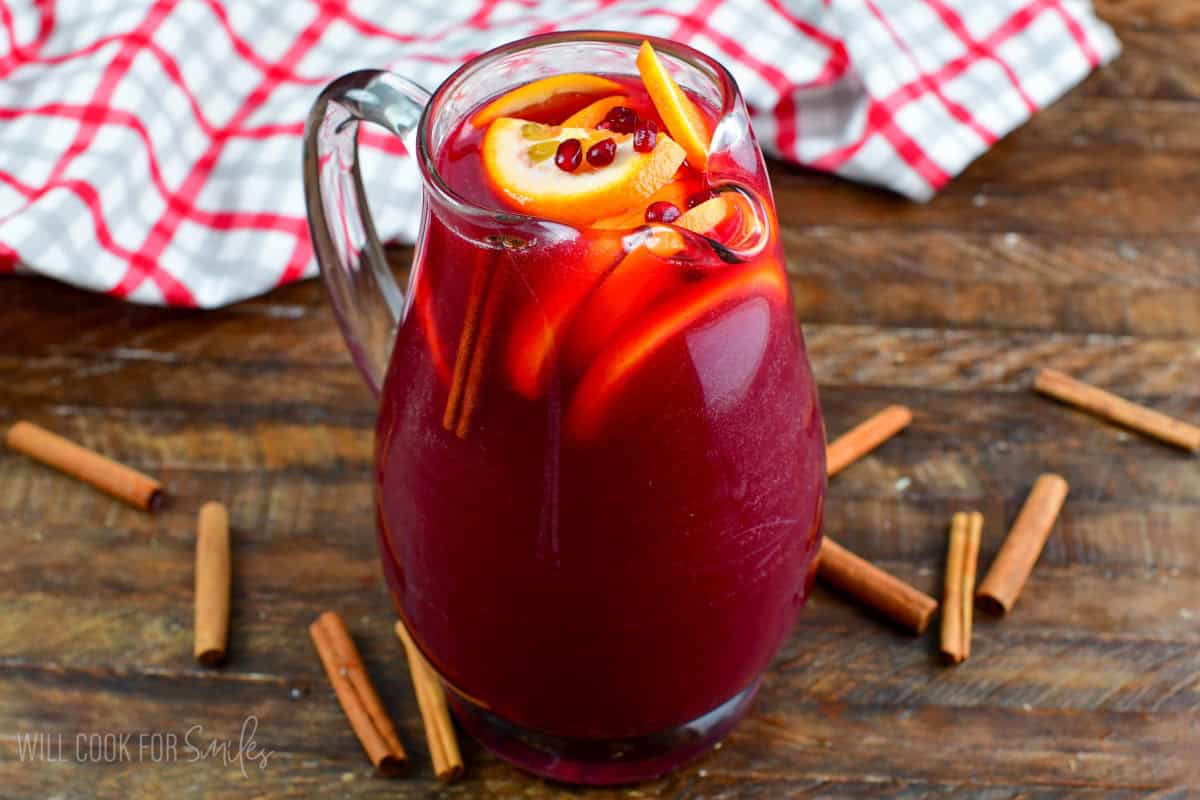 Christmas punch in a pitcher with oranges and pomegranate seeds, and cinnamon sticks.