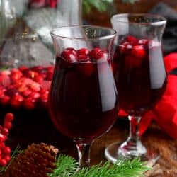 two glasses of cranberry sangria with cranberries and a pitcher behind.