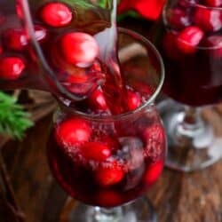 pouring cranberry sangria into the glass with some cranberries.