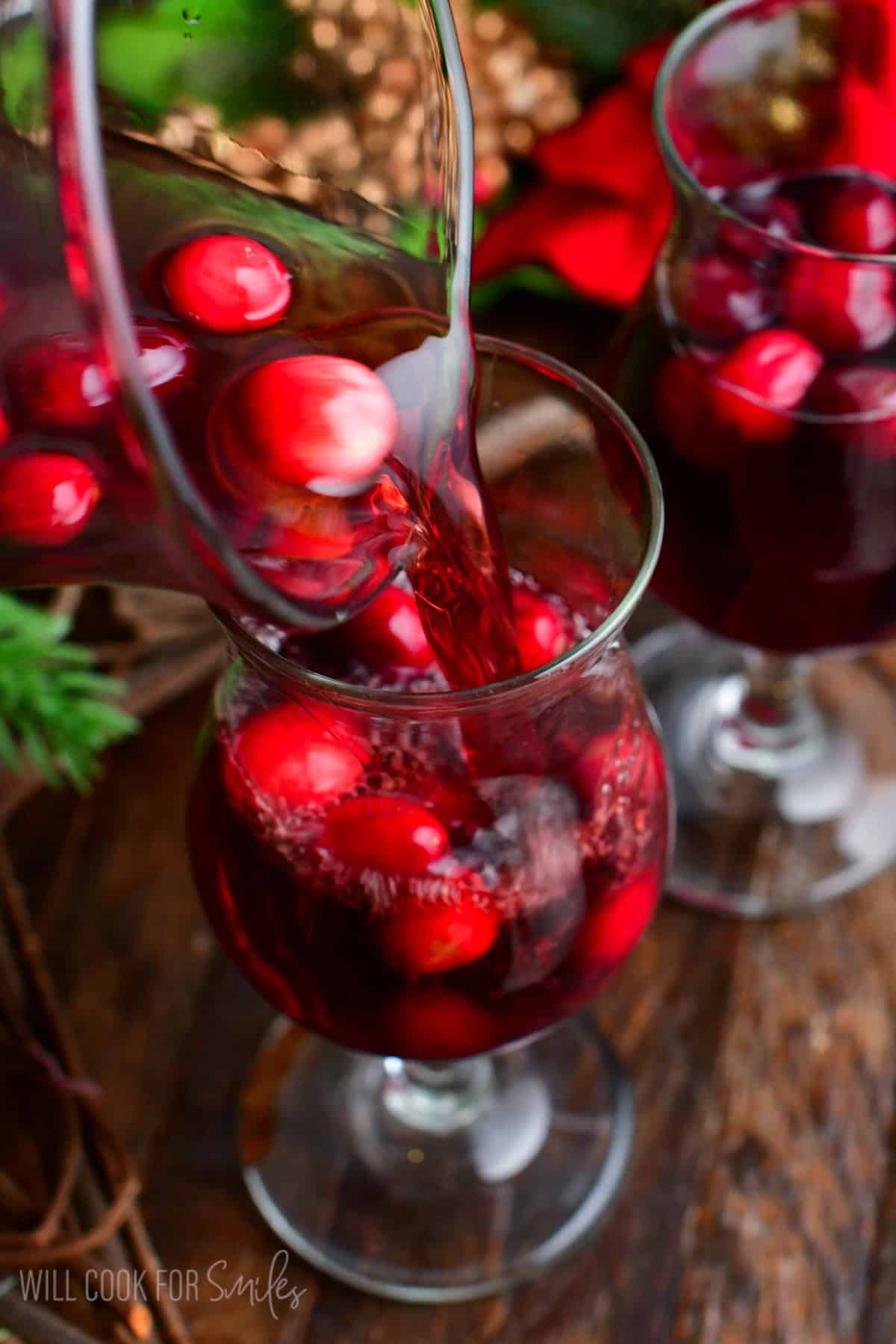 pouring cranberry sangria into the glass with some cranberries.