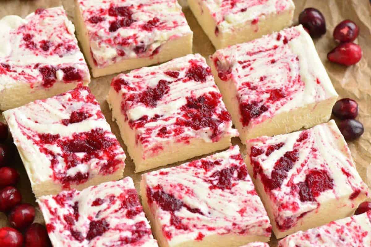 Cranberry White chocolate fudge cut into squares on a parchement paper with fresh cranberries around it.