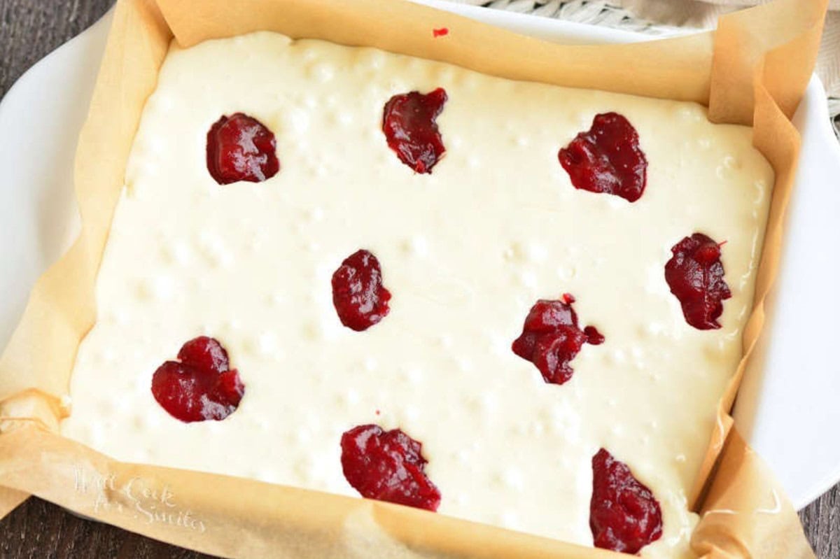 Cranberry fudge mixture with dollops of cranberry jam in a baking dish.