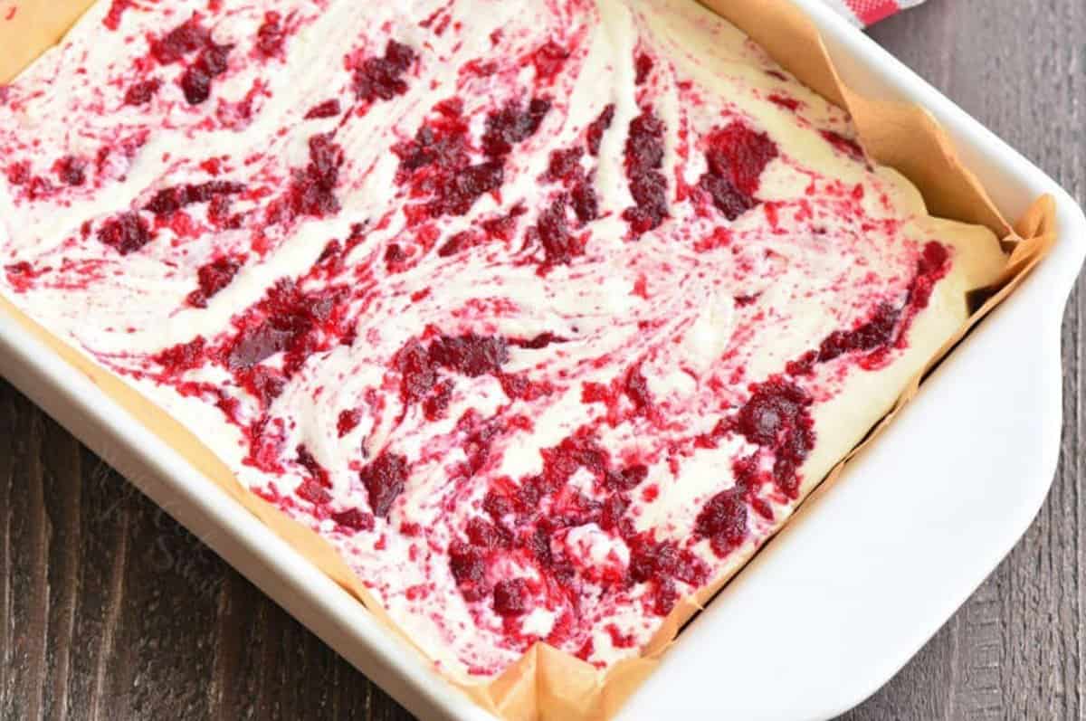 Cranberry fudge mixture with cranberry jam swirled in it in a a parchment lined baking dish.