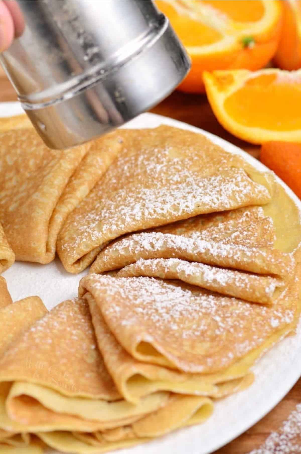 adding powdered sugar to folded crepes on a plate.