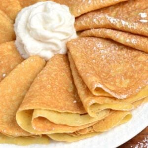 folded crepes arranged on a platter with whipped cream and powdered sugar.