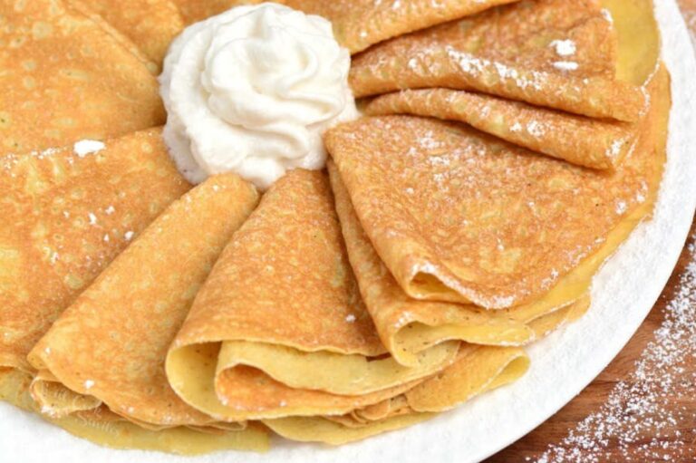 folded crepes arranged on a platter with whipped cream and powdered sugar.