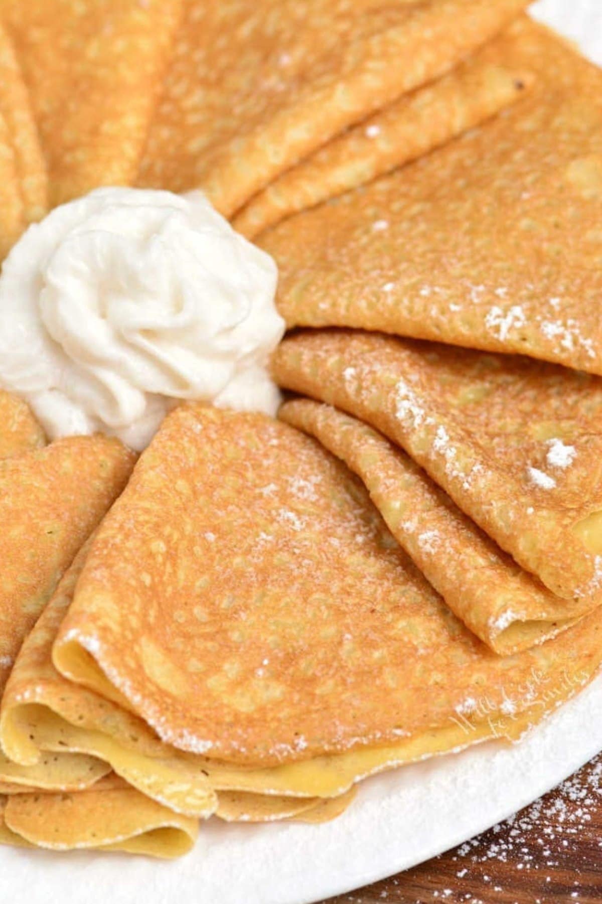 folded crepes arranged on a white plate with whipped cream in the middle.