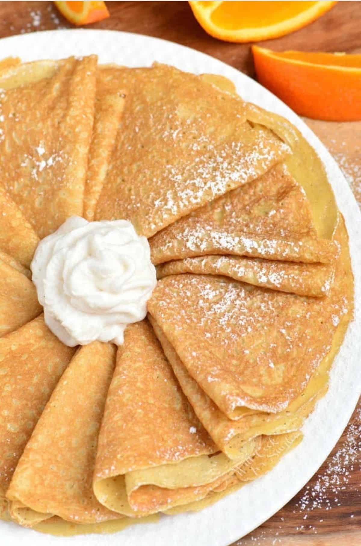 folded crepes arranged on a platter with whipped cream in the middle.