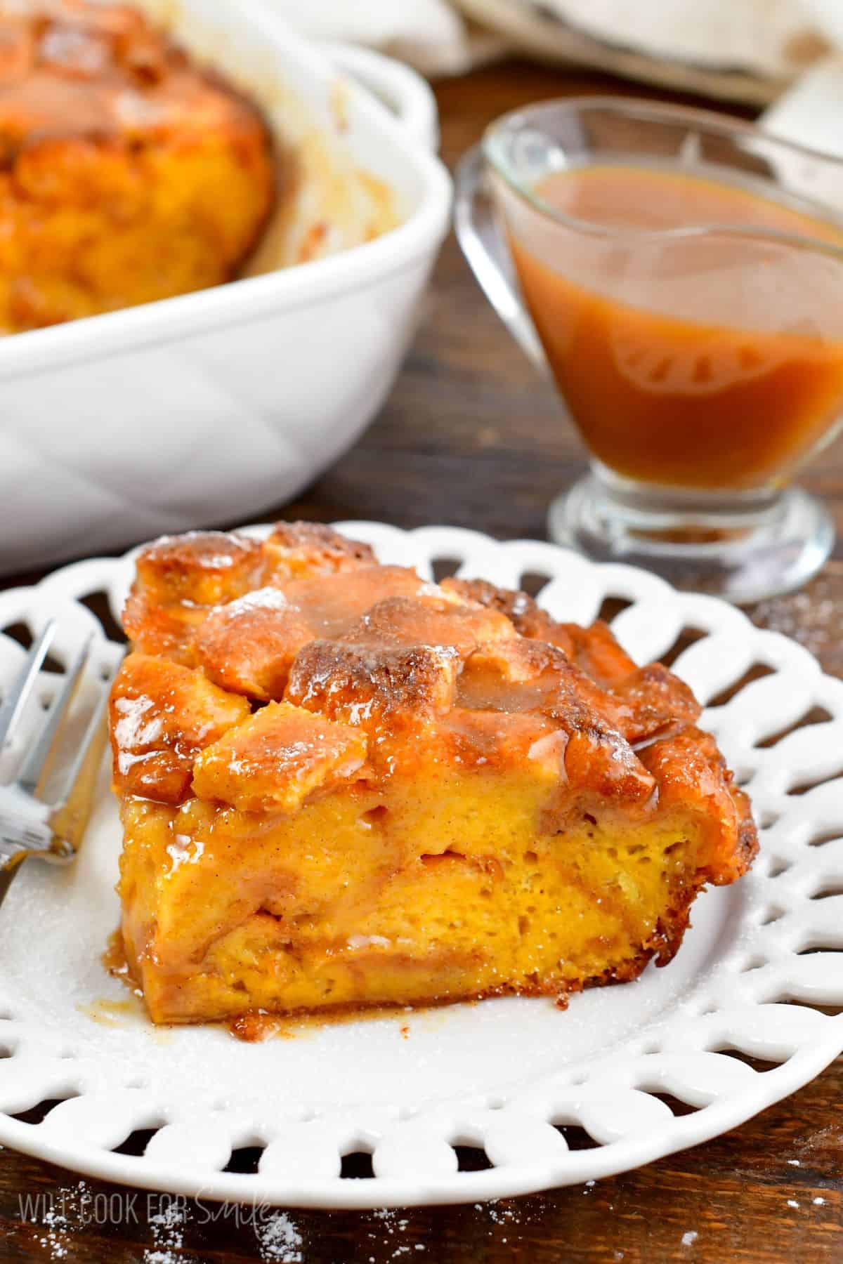 a slice of French toast casserole on the white plate with a fork and more sauce in saucer.