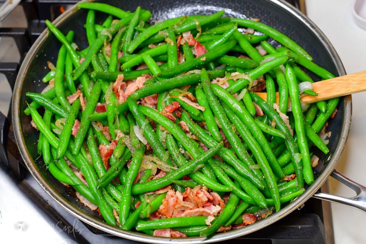 bacon, onions, and green beans cooking in the pan with some salt and pepper seasoning on top.