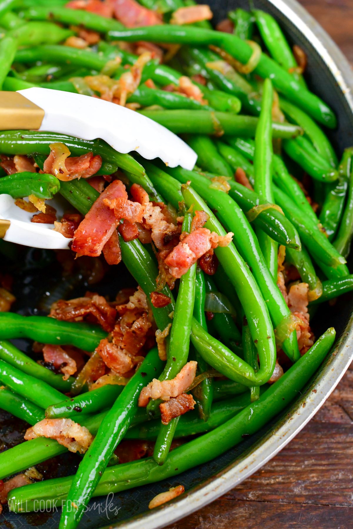 holding some green beans with bacon with white tongs.