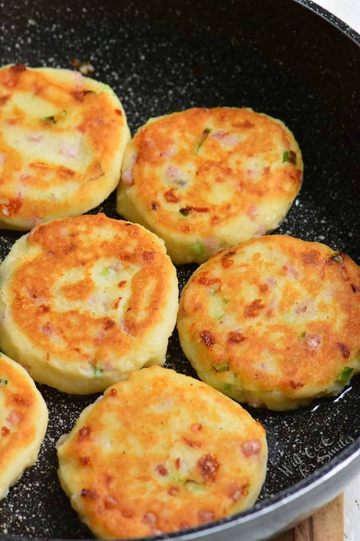 several mashed potato cakes cooking in the pan.