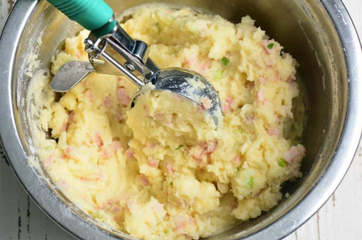 mixture for ham and cheese mashed potato cakes in the mixing bowl with a scoop.