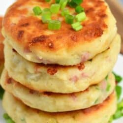 four mashed potato cakes with ham and cheese stacked and topped with chives.