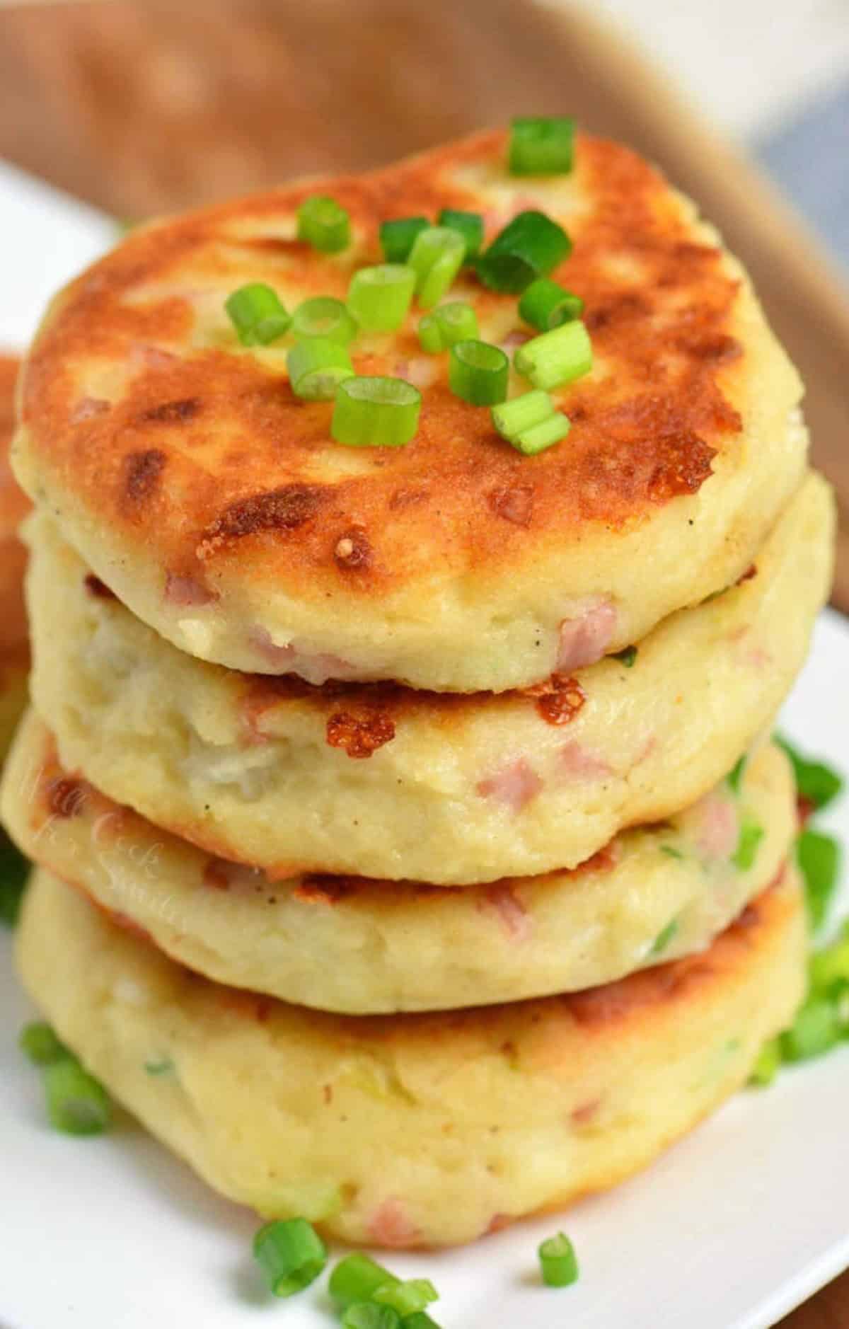 four mashed potato cakes with ham and cheese stacked and topped with chives.