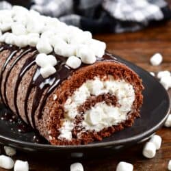 chocolate sponge cake rolled with marshmallow frosting on a black platter.