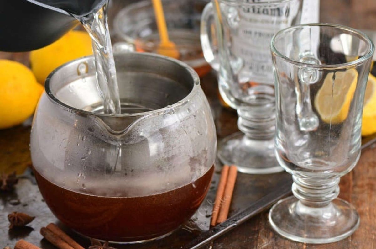 pouring water into the tea pot to make tea next to glass mugs.