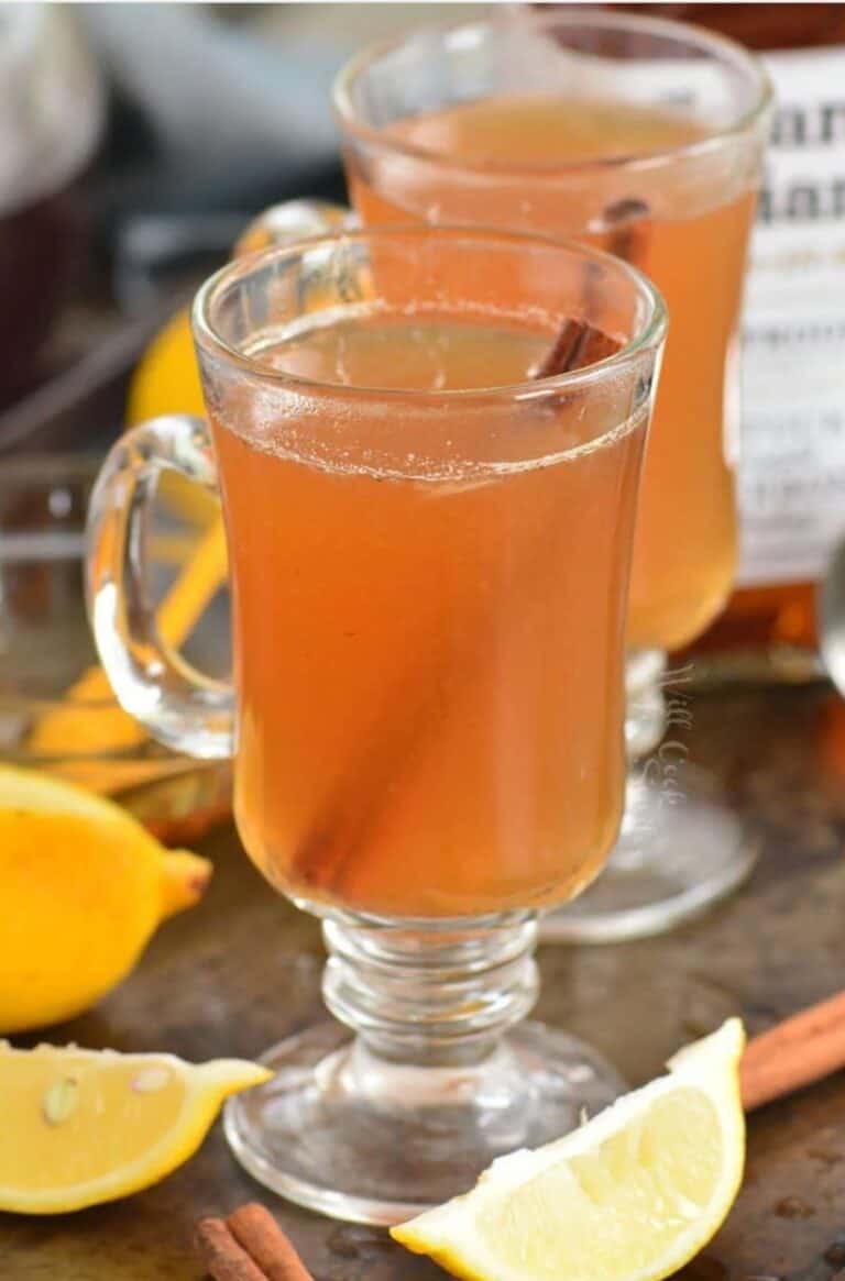 two glass mugs with hot toddies and lemons and cinnamon around.