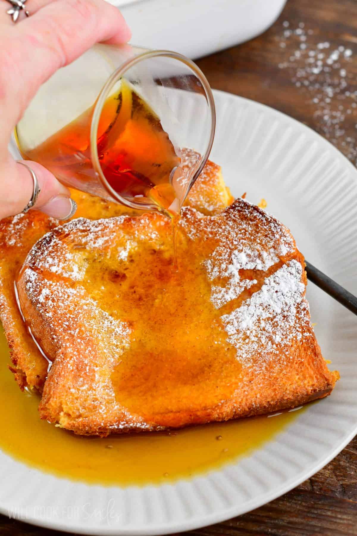 adding maple syrup to the slices of baked French toast on the plate.