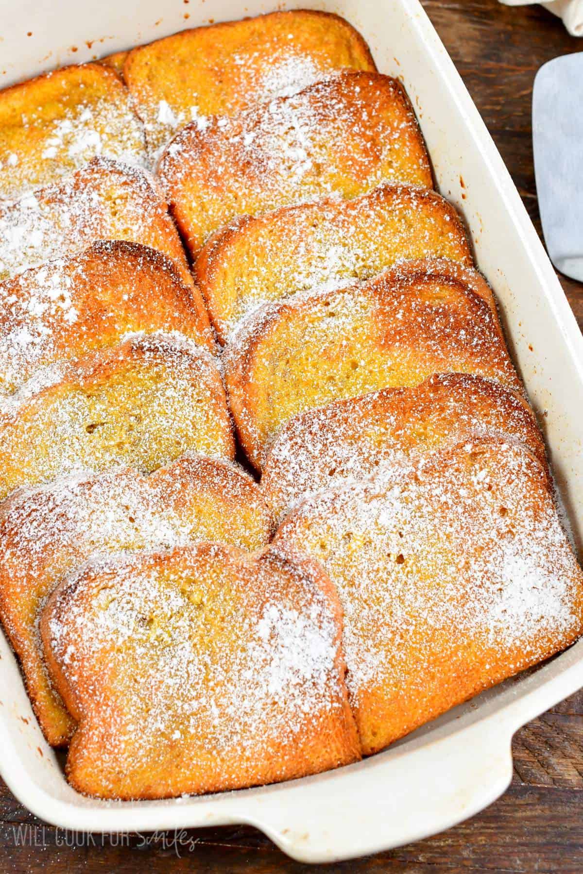 baked French toast casserole in the white baking pan with powdered sugar.