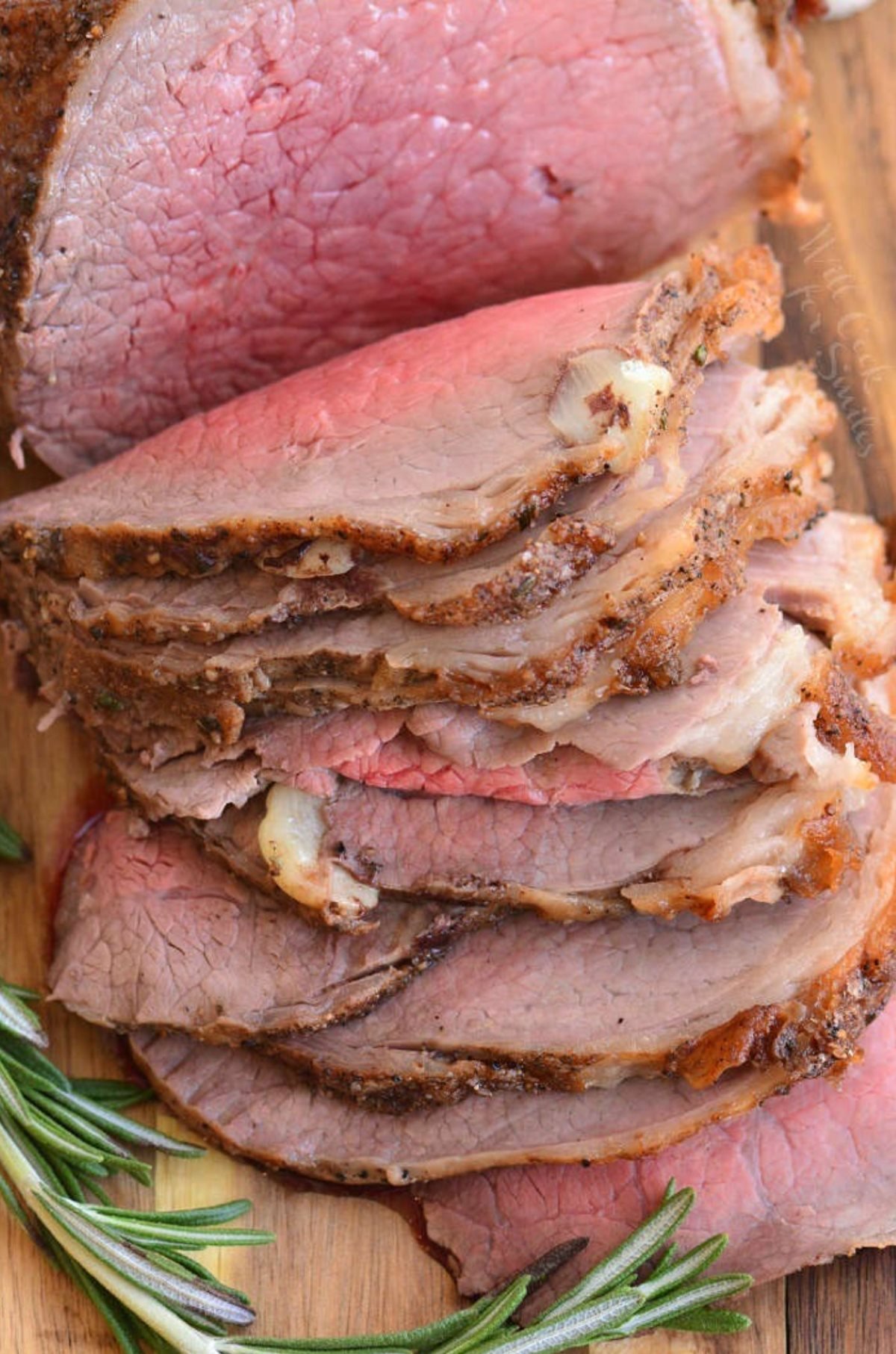 roast beef with slices on a cutting board with rosemary around it.