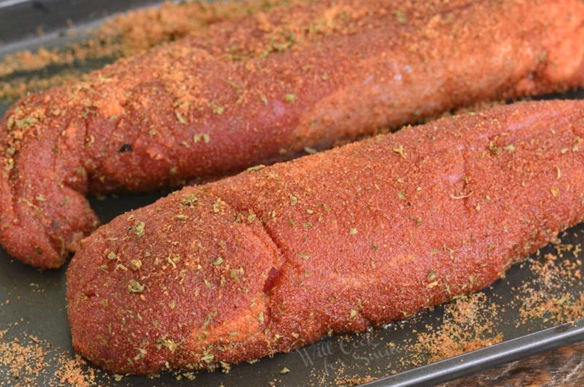 Two uncooked pork tenderloins seasoned and on a baking sheet.