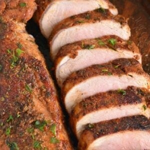 Two roasted pork tenderloins one sliced and one unsliced on a cutting board.