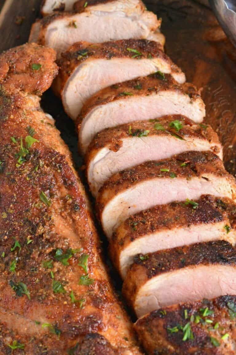 Two roasted pork tenderloins one sliced and one unsliced on a cutting board.