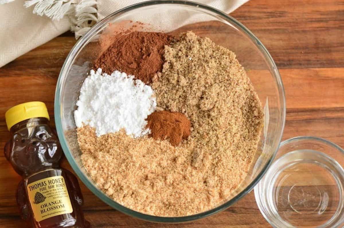 ingredients to make rum balls in a clear bowl and honey and clear liquid next to it.