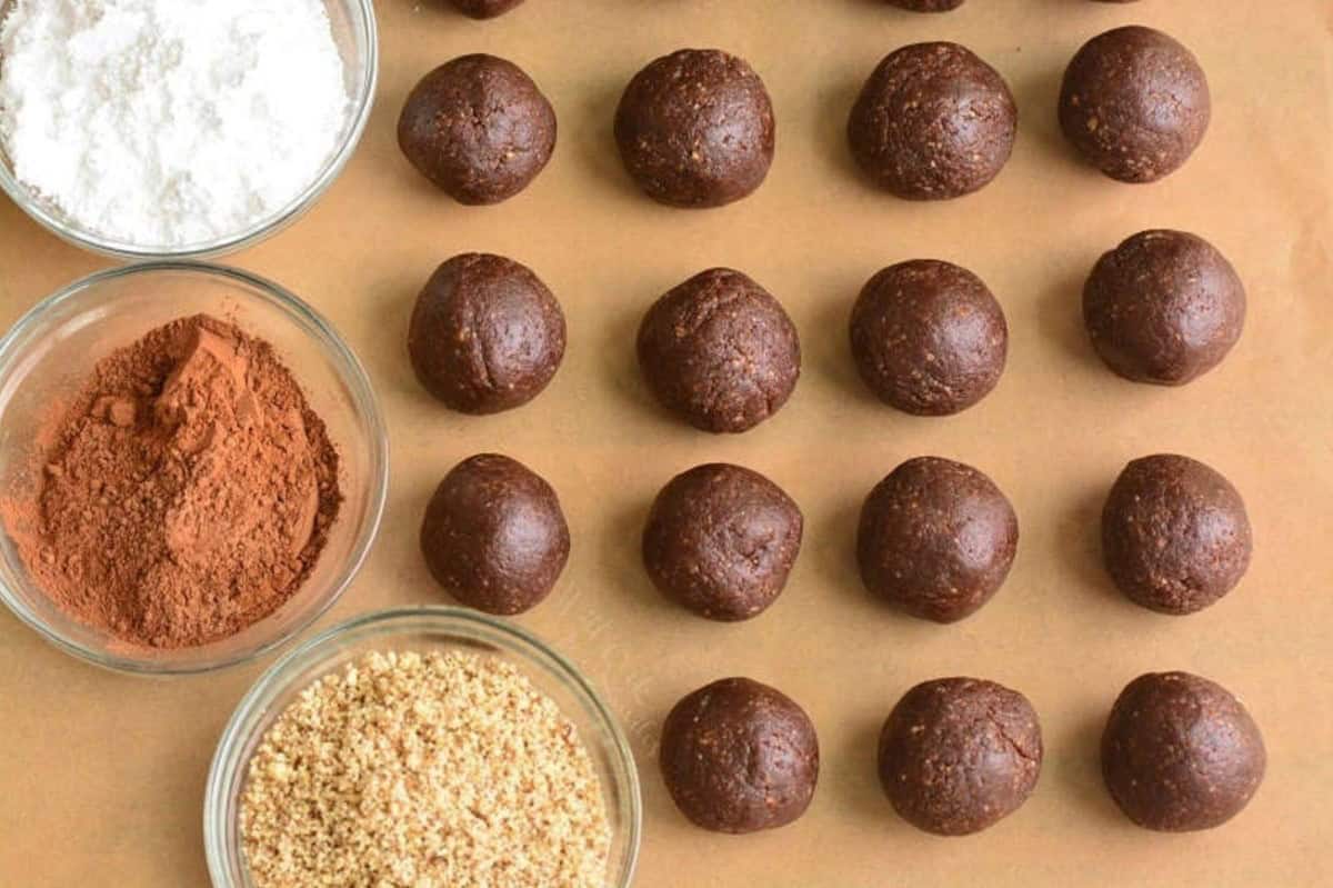 rolled rum balls next to three options for toppings in small bowls.