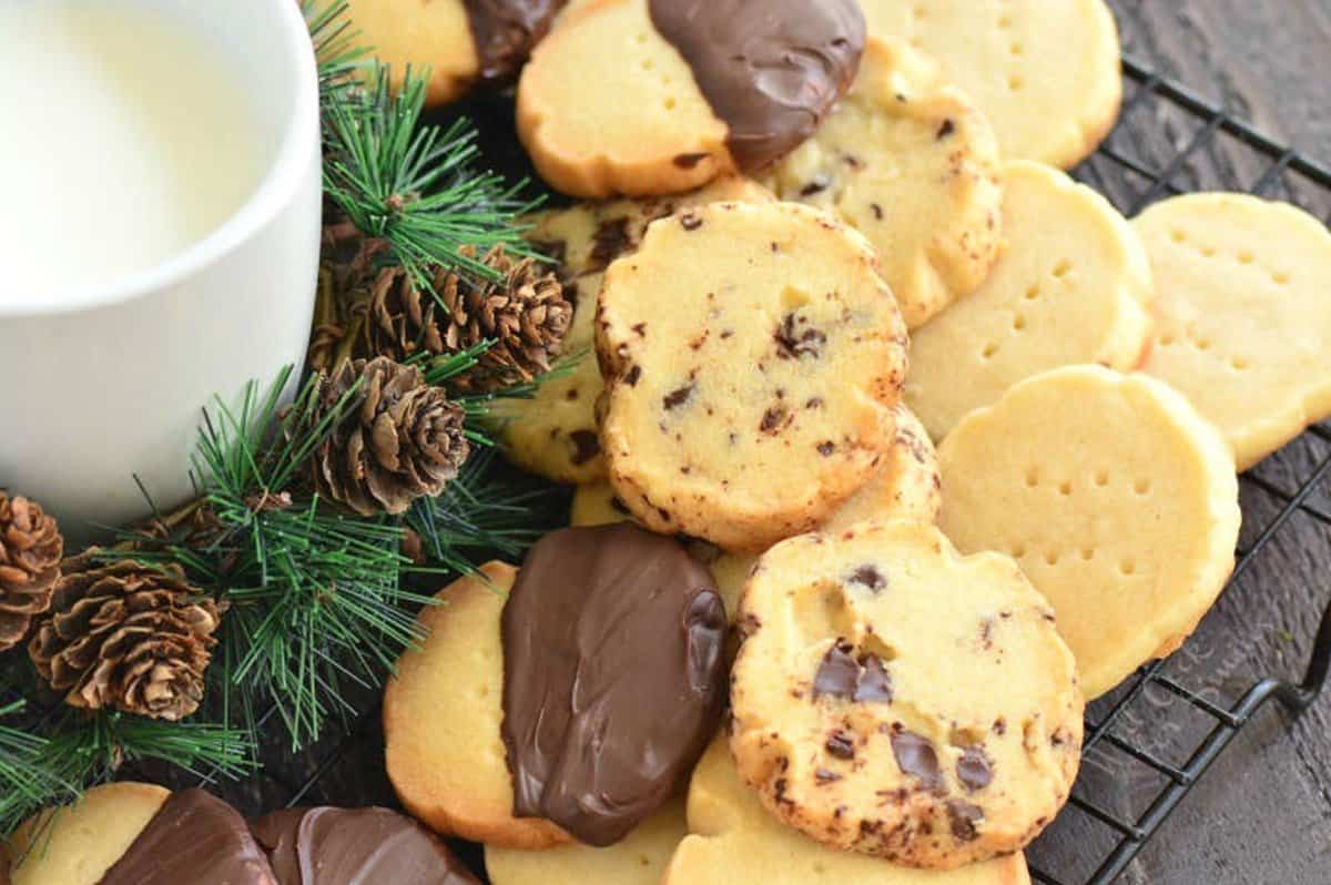 Three kinds of shortbread cookies on a wire rack with a pinecone decor to the left side.