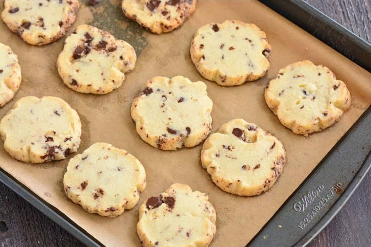 Shortbread cookies with chocolate chunks on a parchment paper lined baking sheet.