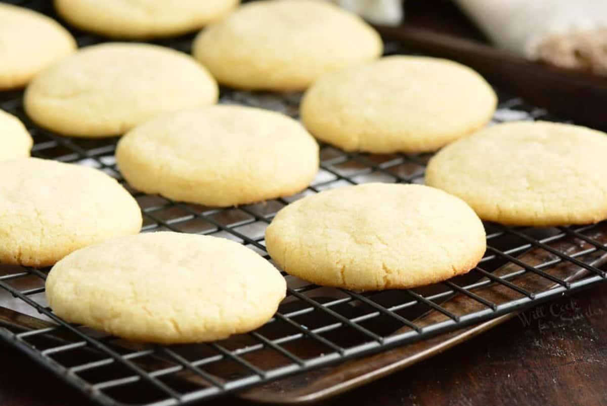 Sugar cookies cooling on a wire wrack stacked on top of a baking sheet.