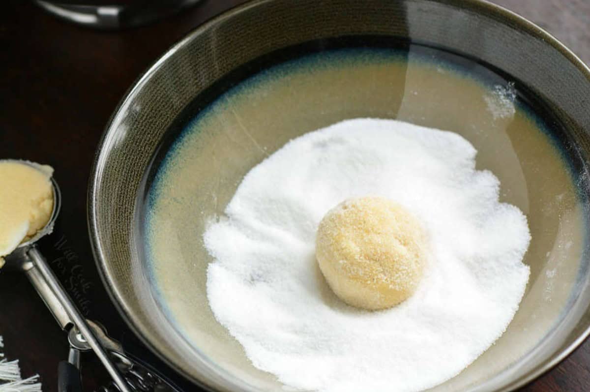 rolling a ball of sugar cookie dough in a bowl of sugar.