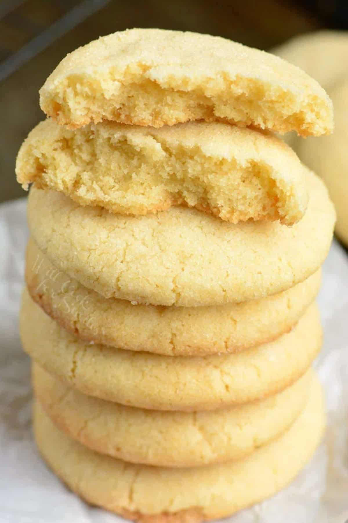 Sugar cookies stacked up on wax paper with the top one broke in half.