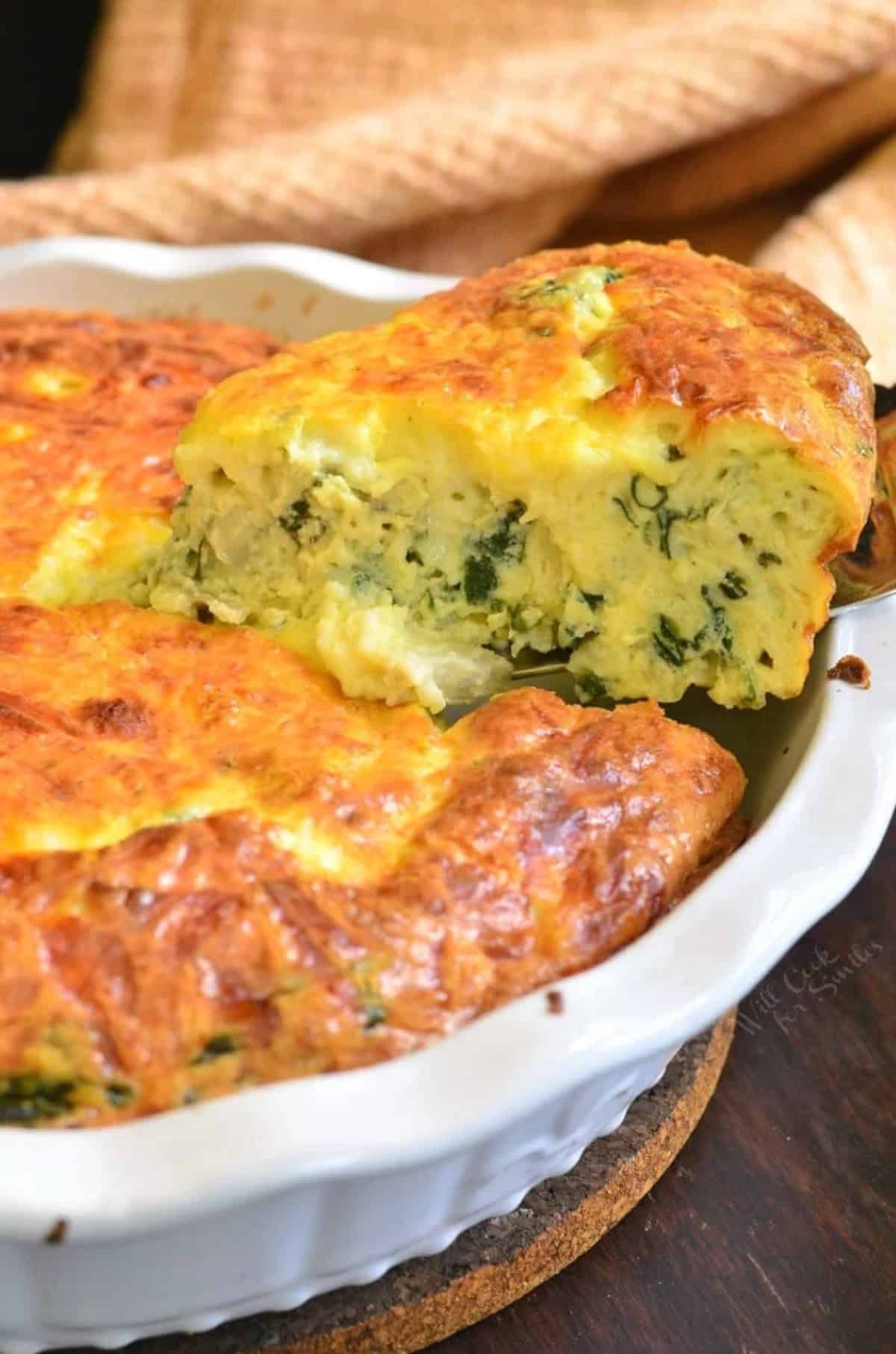 pulling out a slice of spinach artichoke crustless quiche from the baking dish.