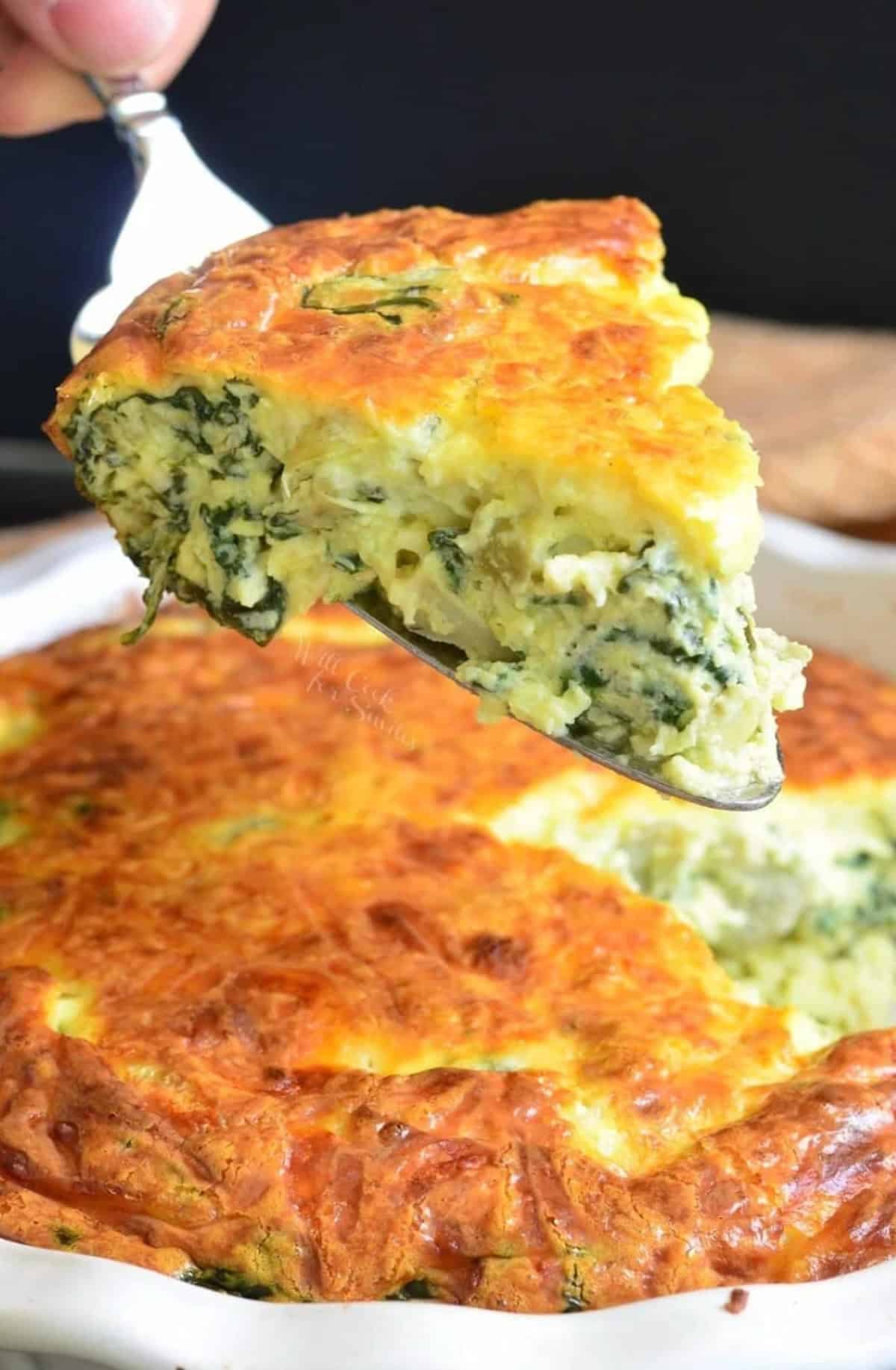 holding a slice of spinach artichoke crustless quiche over the baking dish.