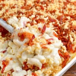 scooping out some mac and cheese with panko topping from baking the pan with silver serving spoon.