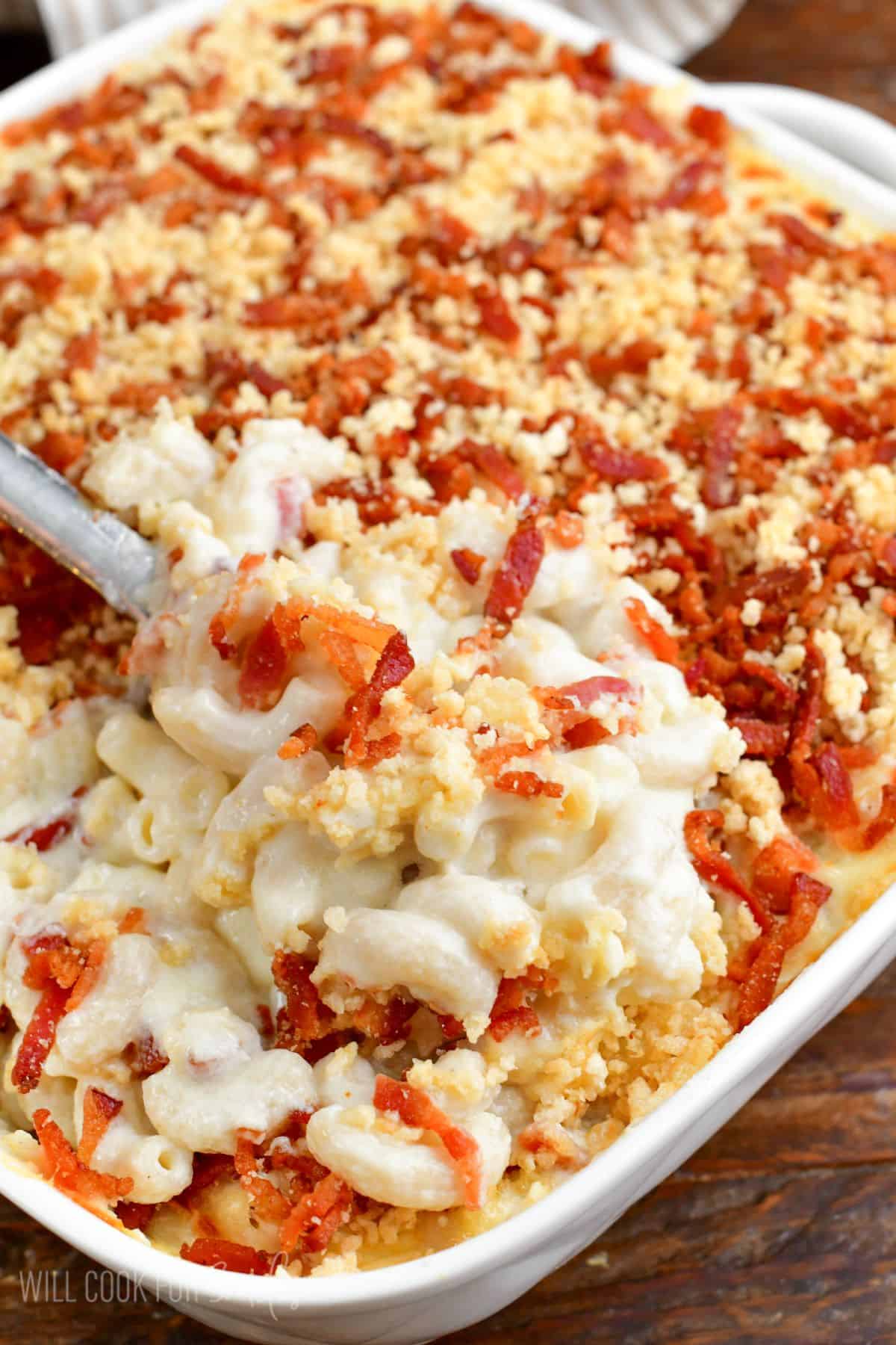 scooping out some mac and cheese with panko topping from baking the pan with silver serving spoon.