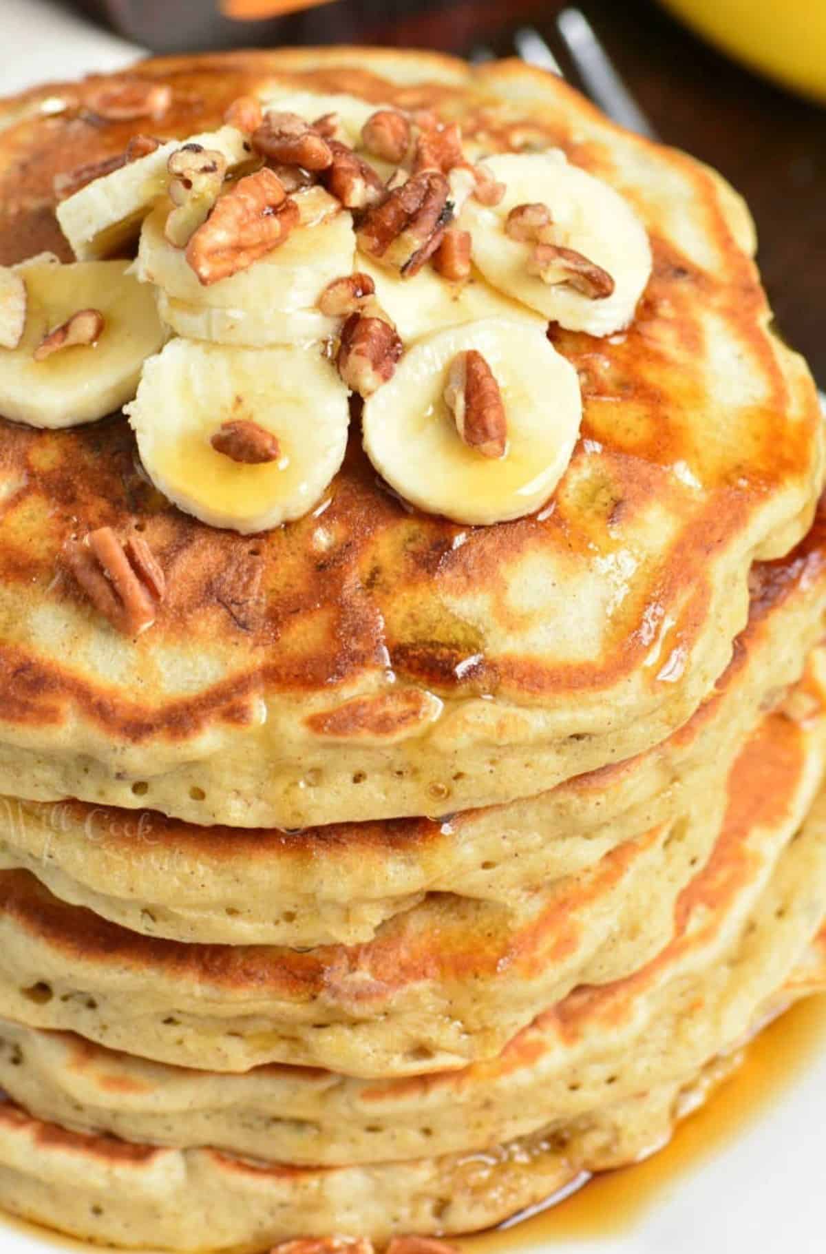 stack of banana pancakes topped with sliced bananas, pecans, and maple.