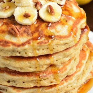 stack of five banana pancakes topped with bananas, nuts, and maple.