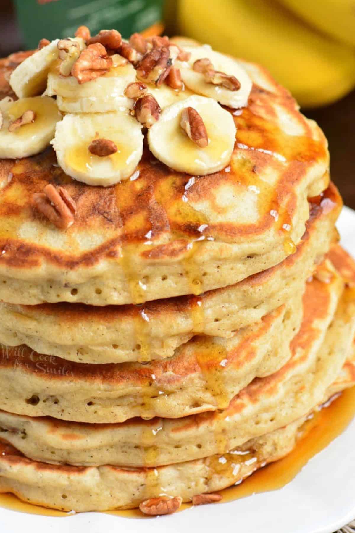 stack of five banana pancakes topped with bananas, nuts, and maple.