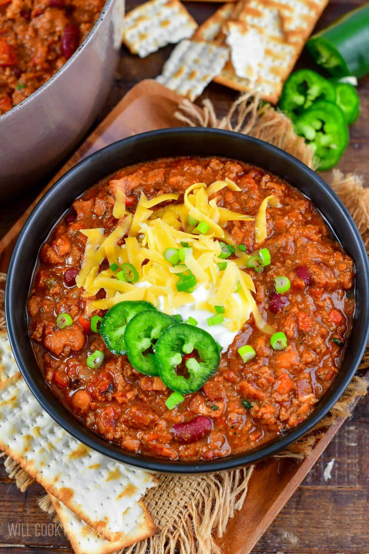 beef chili in a black bowl topped with sour cream, cheese, onions, and jalapenos.