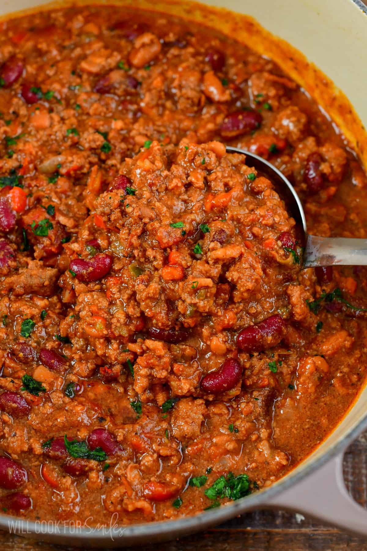 scooping beef chili from the pot with a silver ladle.