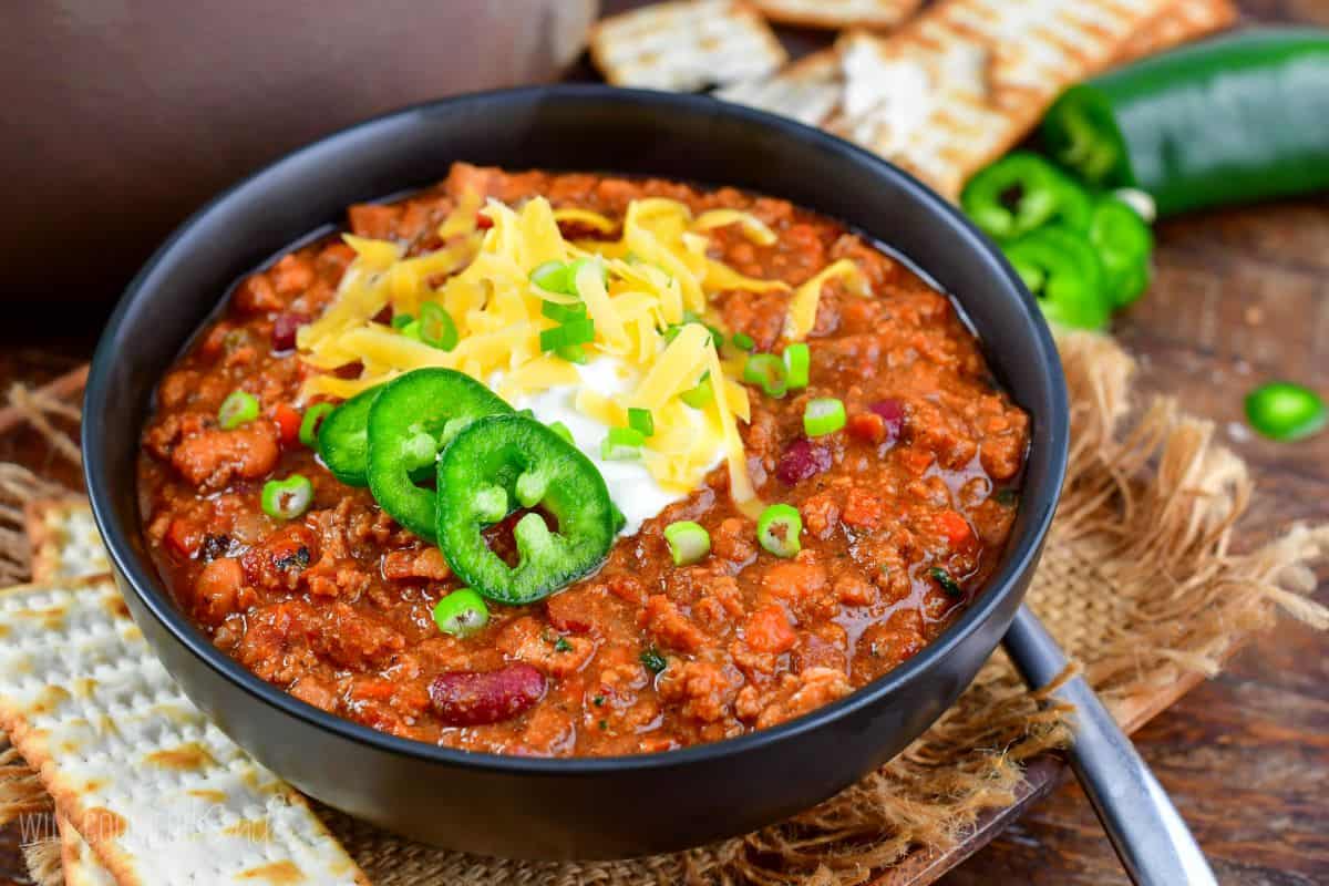 beef chili in a bowl topped with sour cream, cheese, onions, and jalapenos and spoon next to it.