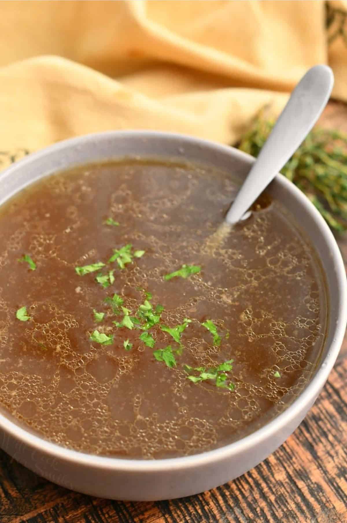 a bowl of beef stock with some parsley garnish and a spoon.