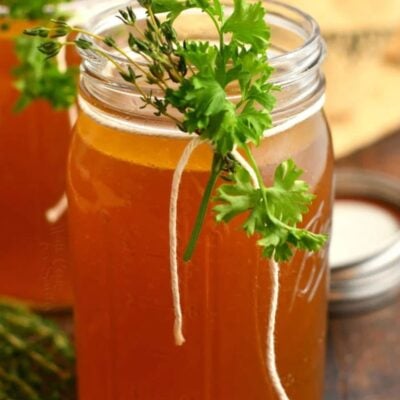 homemade beef stock in glass mason jars with some herbs tied to it.